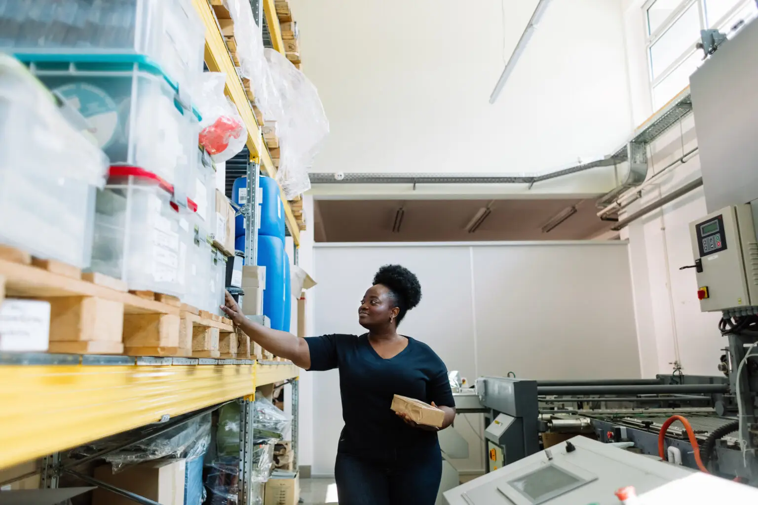 Woman in black top reaching for items on warehouse shelving