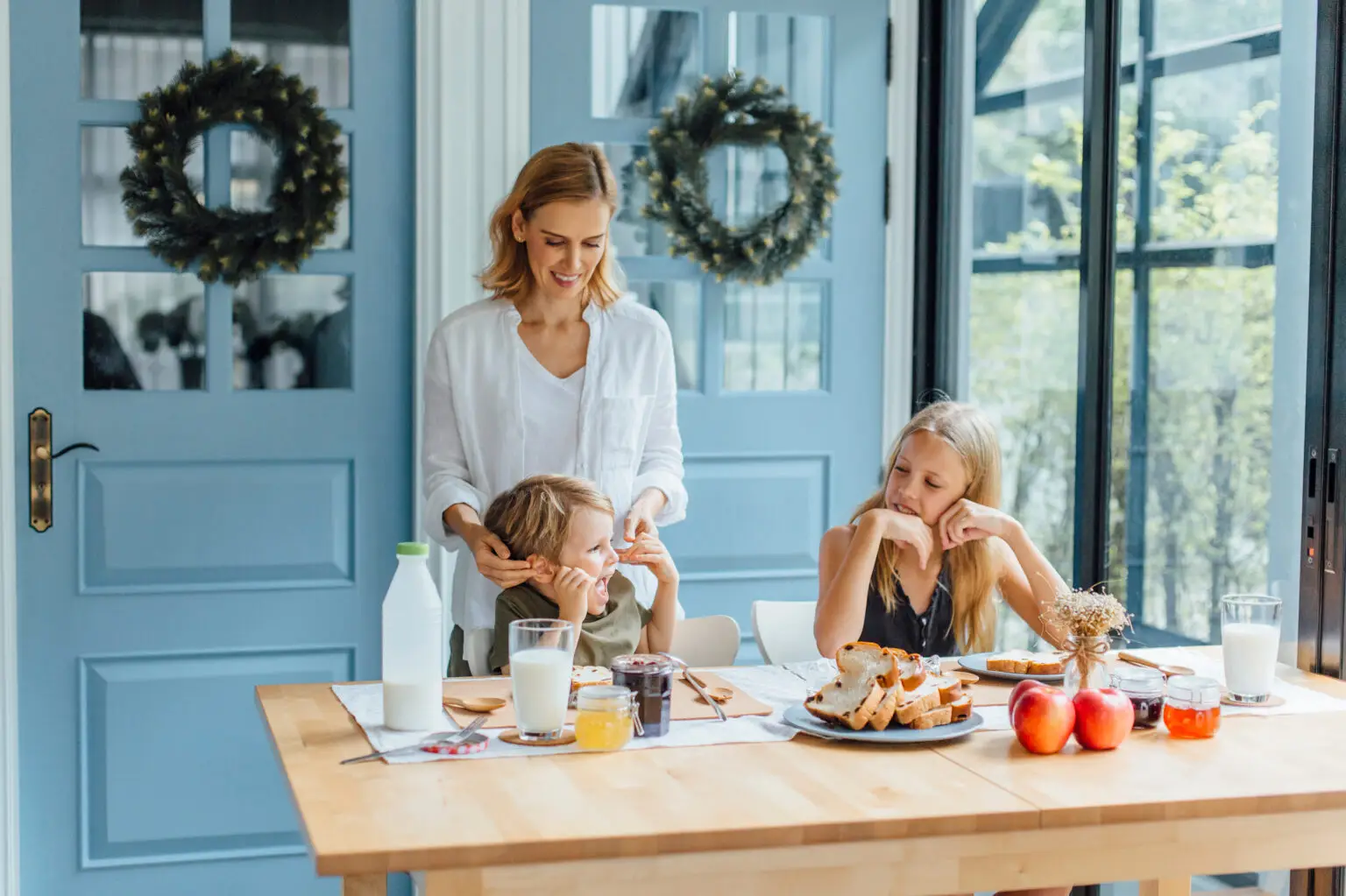 Mother standing with two children at kitchen table during breakfast