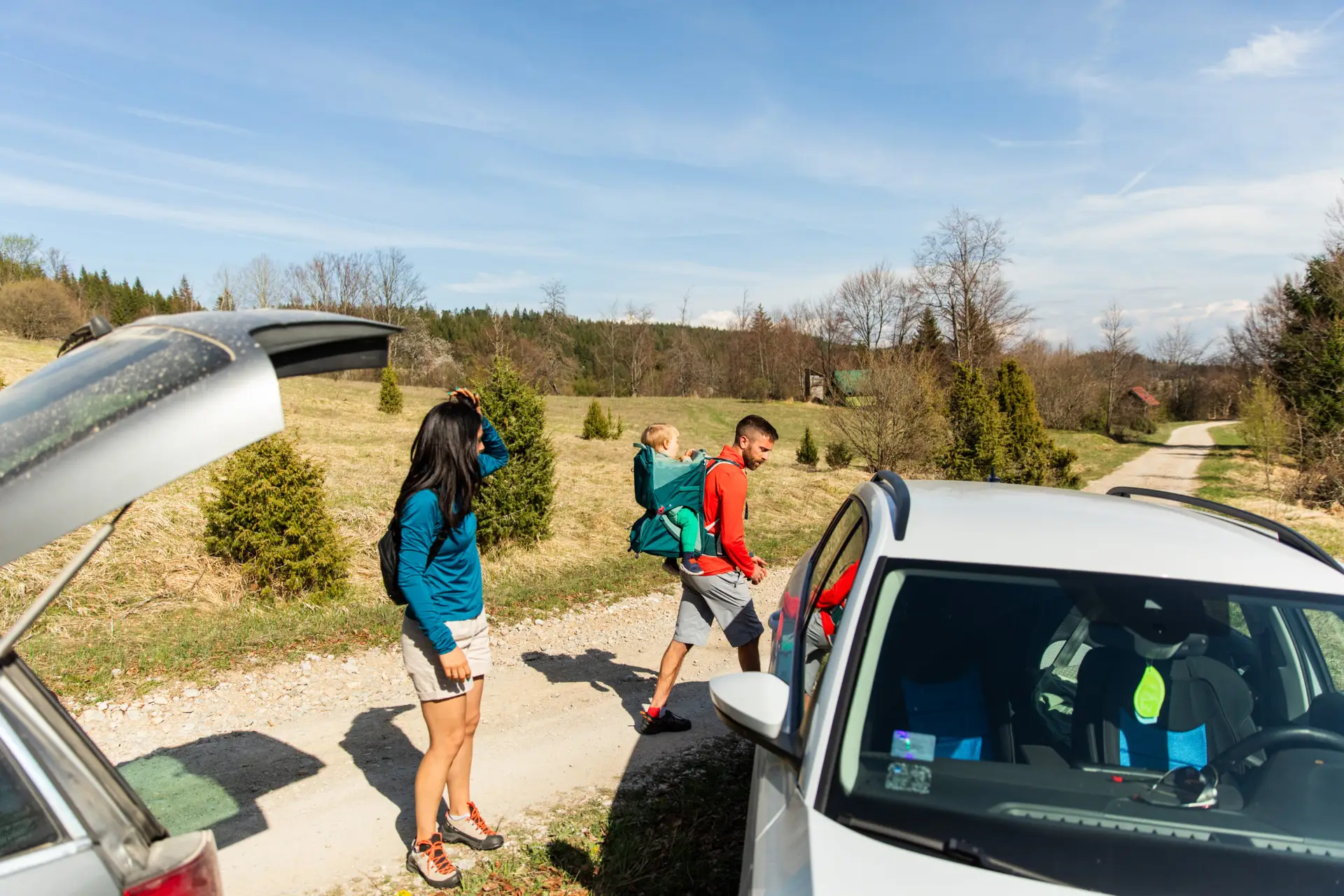 Couple with baby in backpack carrier unloading car for hike