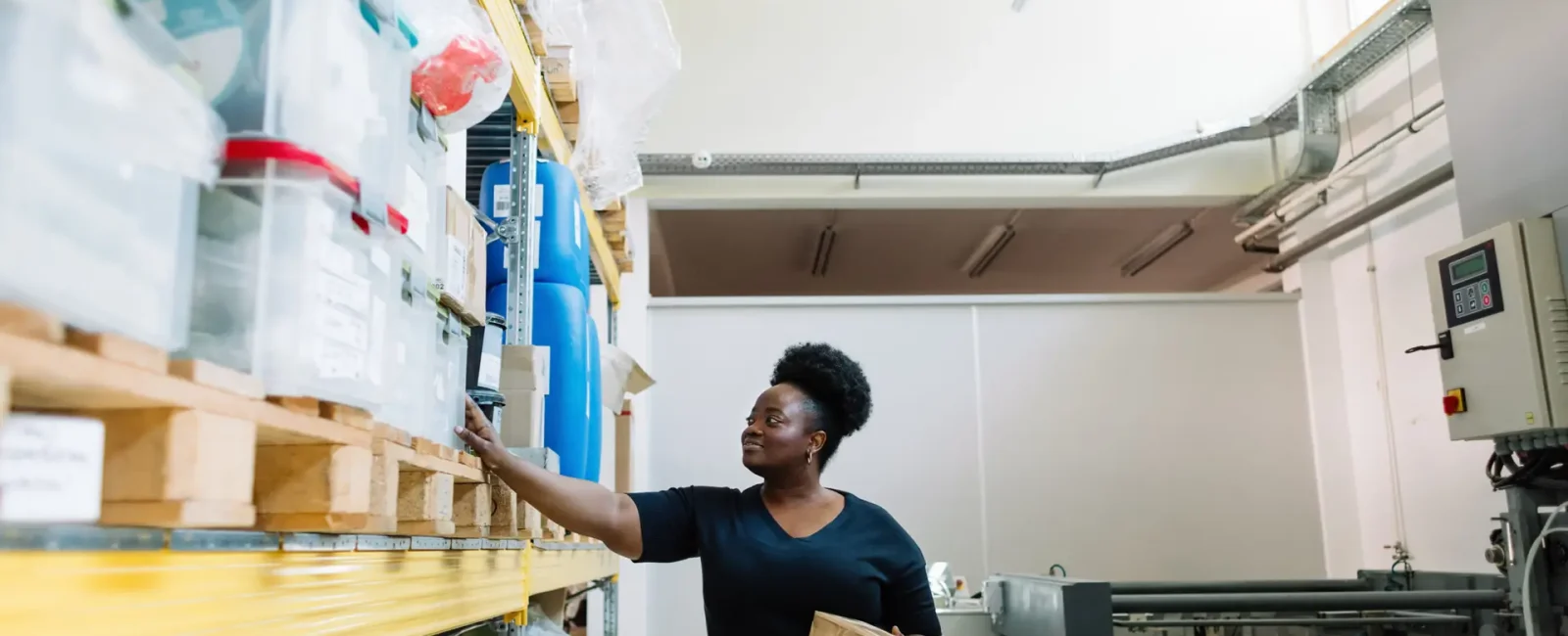 Woman in black top reaching for items on warehouse shelving