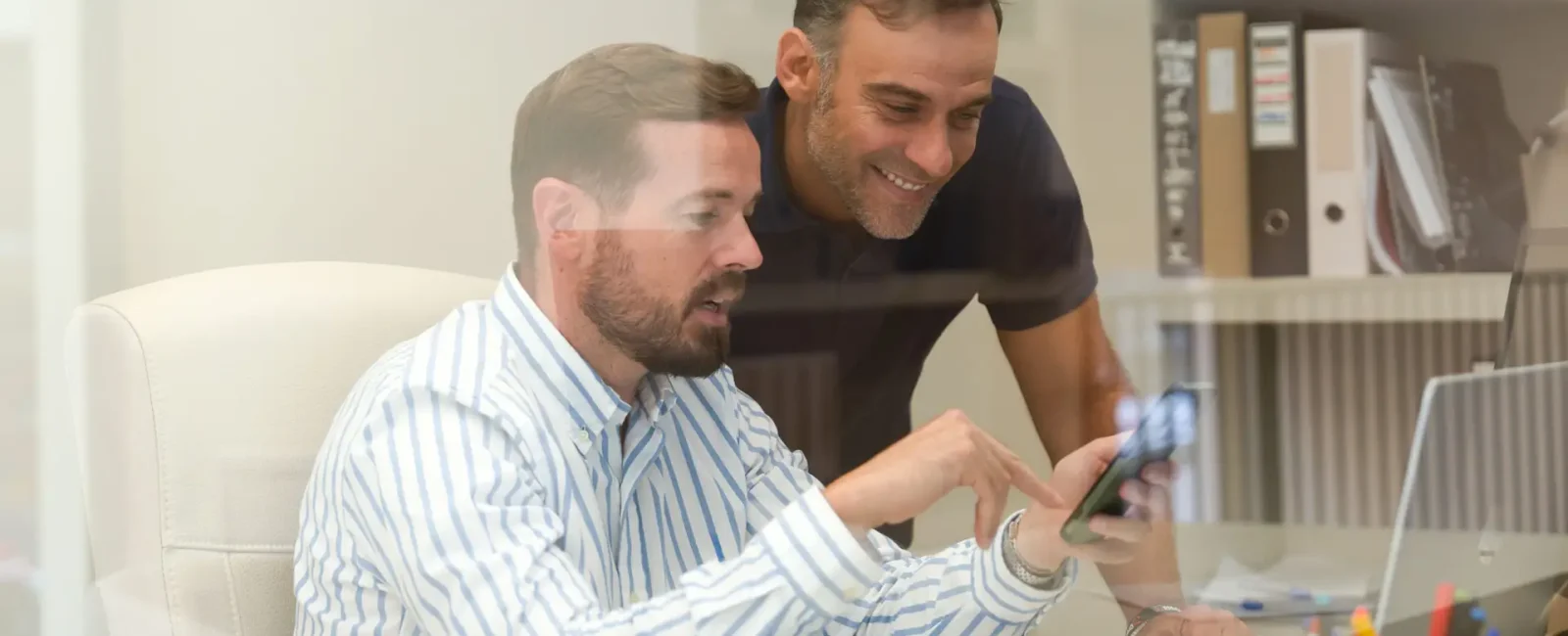 Two men reviewing information on phone together at office desk