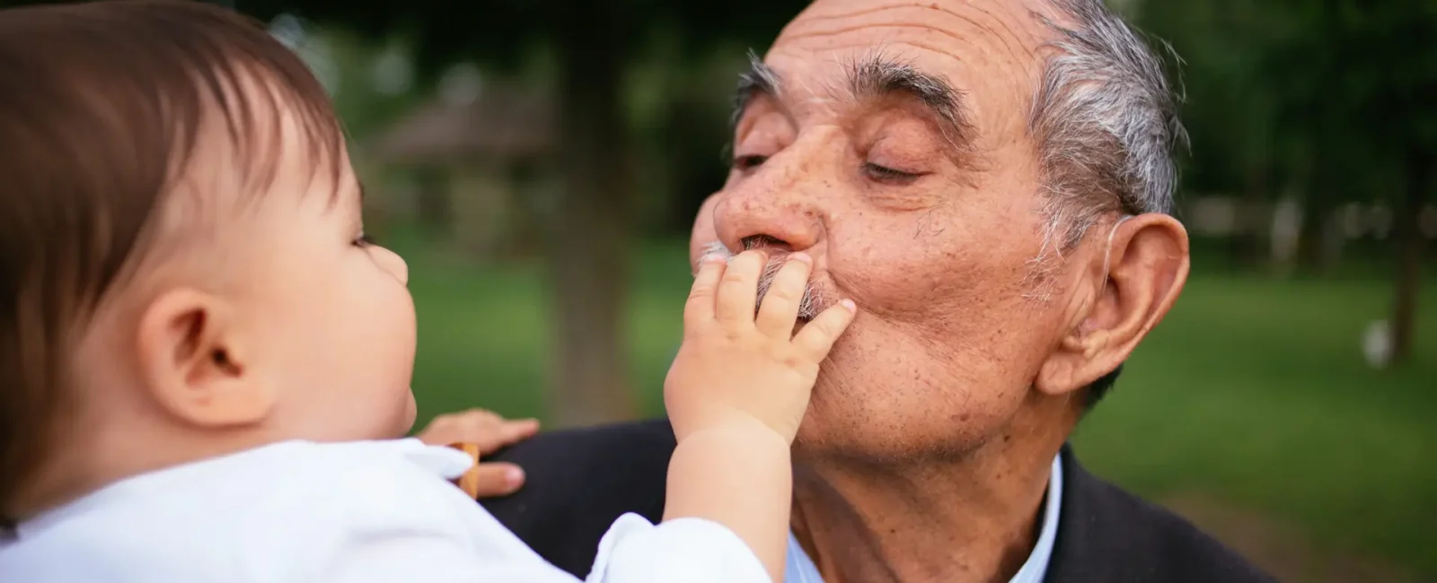 Elderly man in suit holding infant outdoors in garden