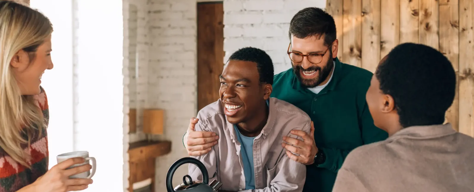 Four friends laughing together around kitchen table with coffee