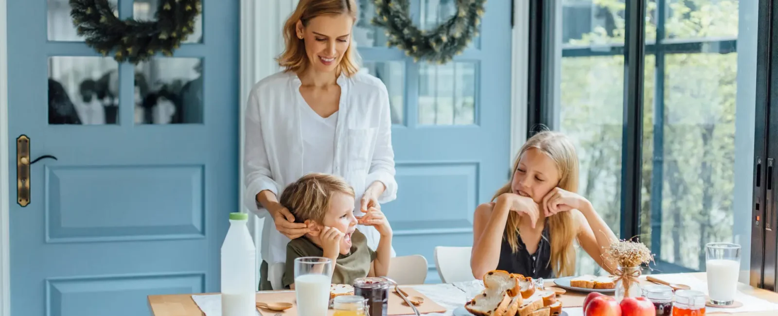 Mother standing with two children at kitchen table during breakfast